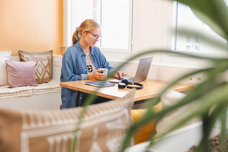 Jeune femme travaillant dans un espace cosy, avec son ordinateur et sa tasse de café